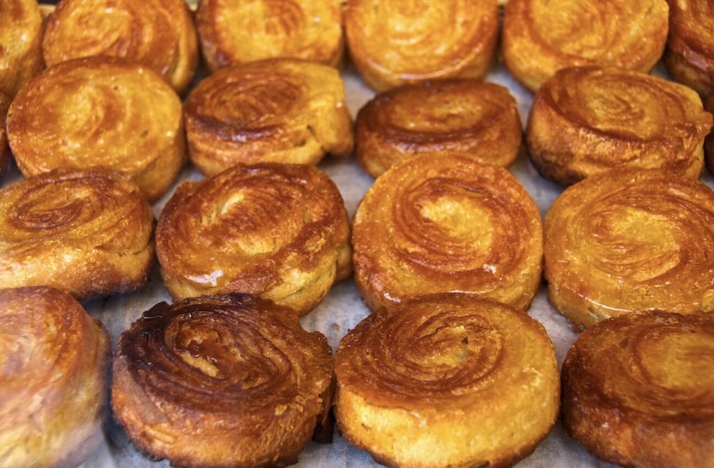 Rows of golden-brown Kouign-Amann, a buttery and caramelized pastry from Brittany, showcasing the rich flavors of traditional French foods.