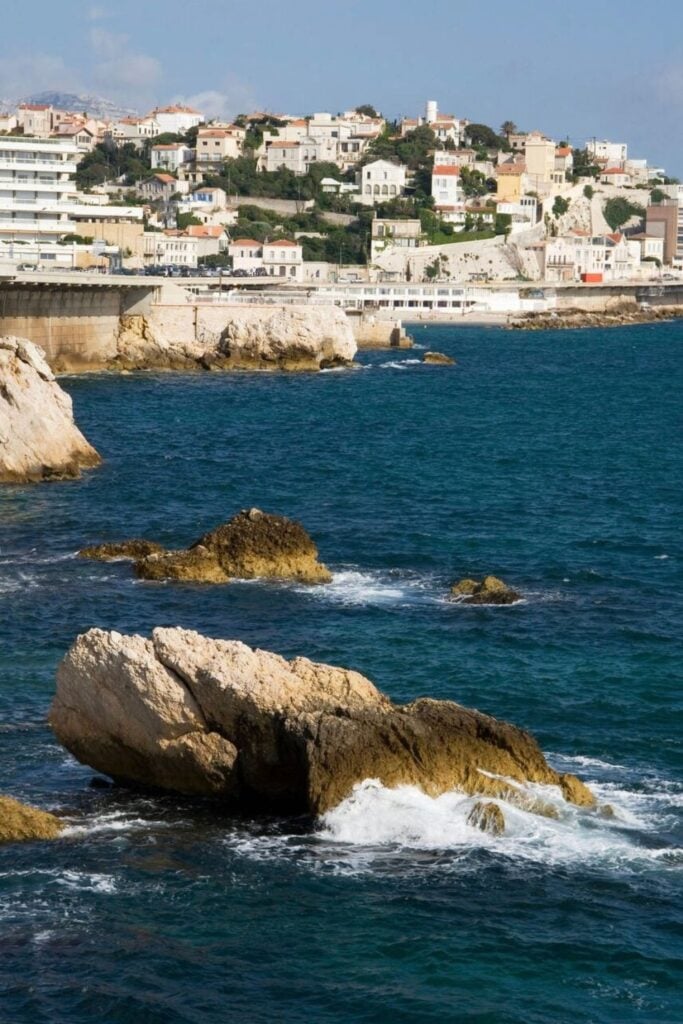 Waves crash against the rugged coastline of Marseille, with picturesque hillside villas overlooking the Mediterranean—exploring the city's stunning seaside views is one of the top things to do in Marseille France.