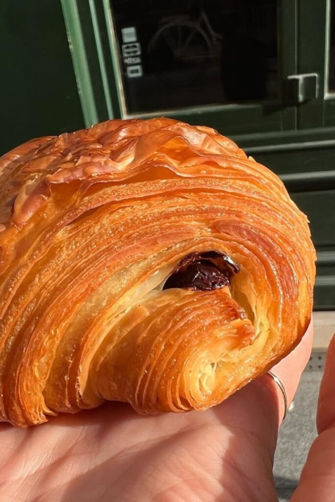 A flaky, golden-brown pain au chocolat with delicate layers of pastry and melted chocolate, capturing the essence of traditional French foods.