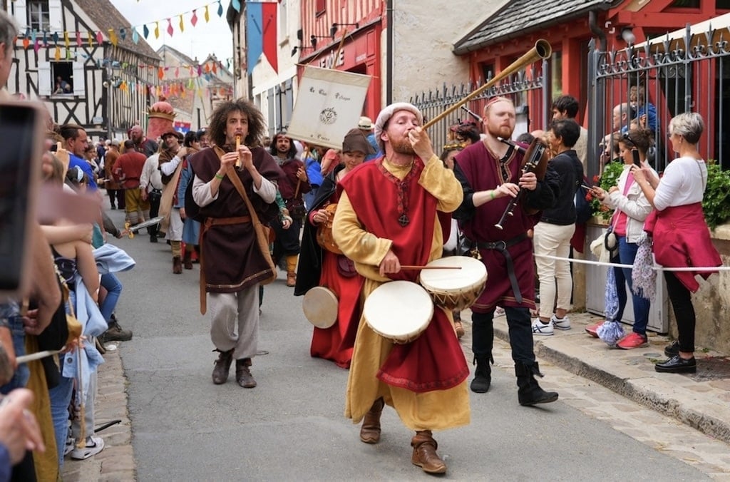 A lively medieval festival with musicians in traditional costumes parading through a charming village, making it a unique cultural experience for day trips from Paris France.