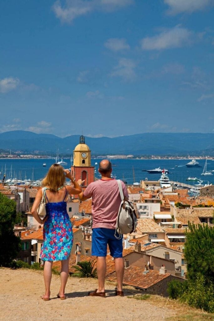 A couple overlooks the rooftops, marina, and iconic clock tower of Saint-Tropez, a popular destination for day trips from Nice, France.