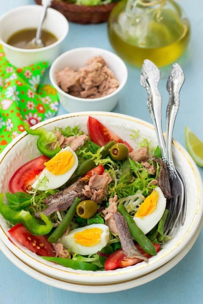 A vibrant salade niçoise, a classic traditional French foods, featuring tuna, anchovies, hard-boiled eggs, tomatoes, green beans, and olives on a bed of fresh greens.