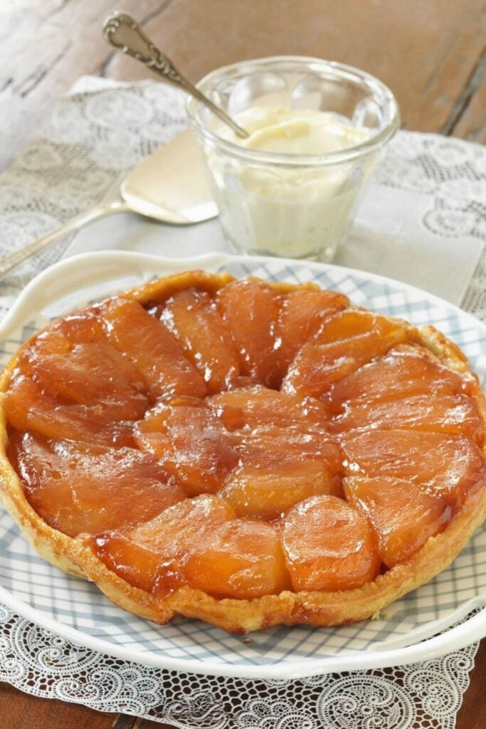 A caramelized tarte Tatin, a beloved traditional French foods, featuring glossy, golden apples atop a flaky pastry, served with a side of crème fraîche.