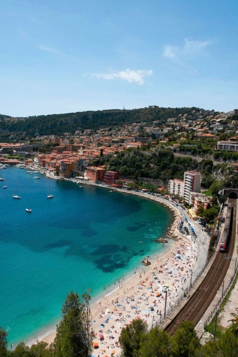 The picturesque coastline of Villefranche-sur-Mer, with its sandy beach, colorful village, and scenic train route, is a favorite spot for day trips from Nice, France.