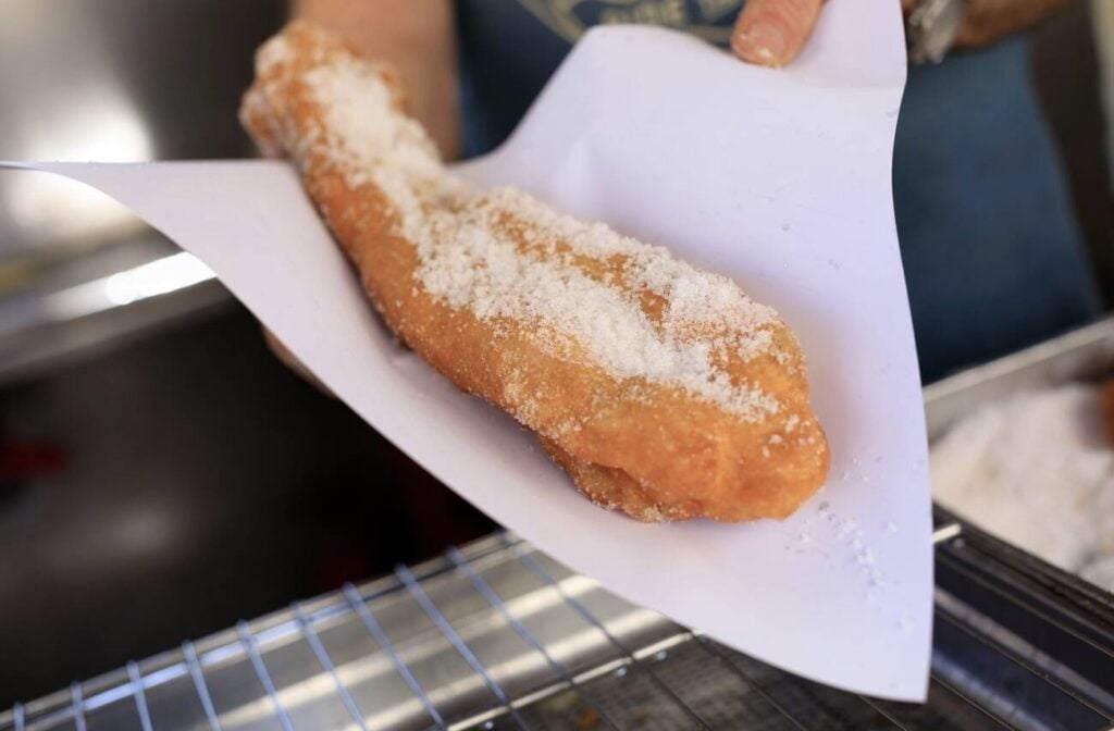 A freshly fried churro-like pastry coated in sugar, served in a paper wrapper—a sweet treat featured in any Marseille Food Guide.