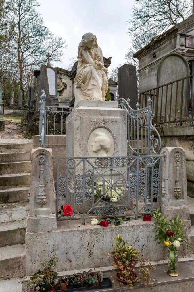 The tomb of Frédéric Chopin at Père Lachaise Cemetery features an elegant marble sculpture of a grieving woman, an engraved portrait of the composer, and offerings of fresh flowers left by admirers.