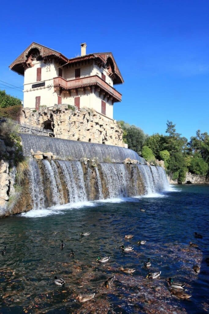 The scenic Cascade de Gairaut in Nice features a charming Swiss-style house perched above a cascading waterfall, with ducks swimming in the clear waters below—an idyllic spot for nature lovers and one of the unique things to do in Nice.