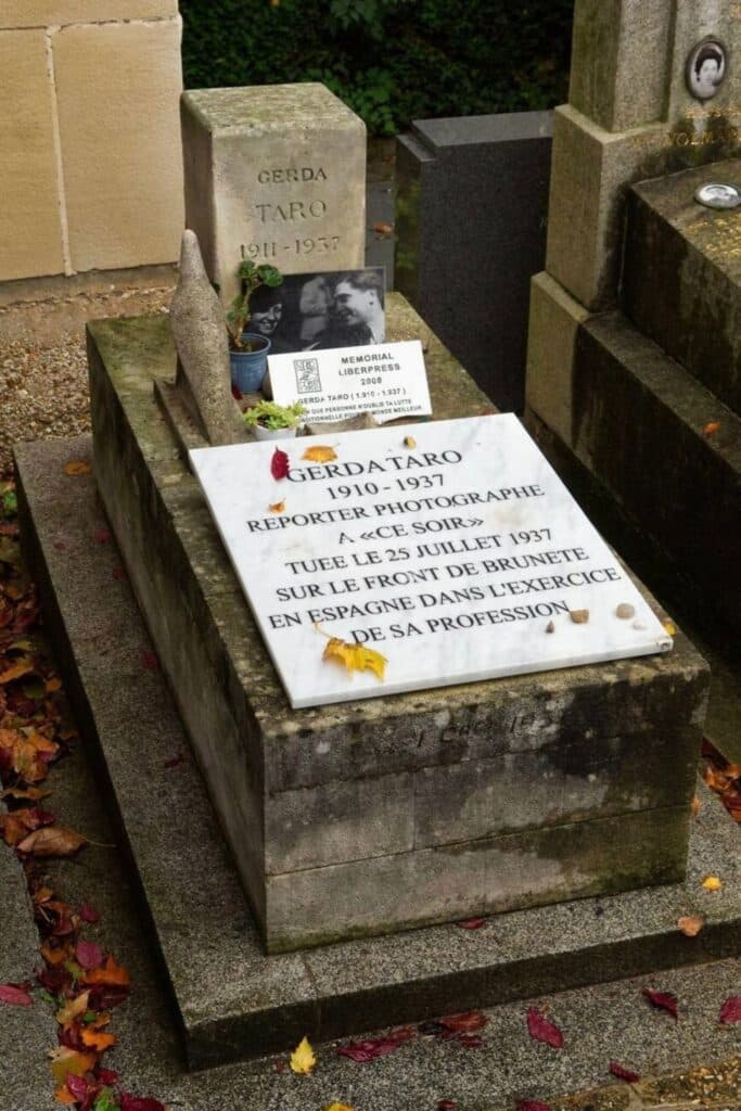 The grave of photojournalist Gerda Taro at Père Lachaise Cemetery features a white marble plaque inscribed with her name and story, accompanied by fallen autumn leaves and a small memorial tribute.