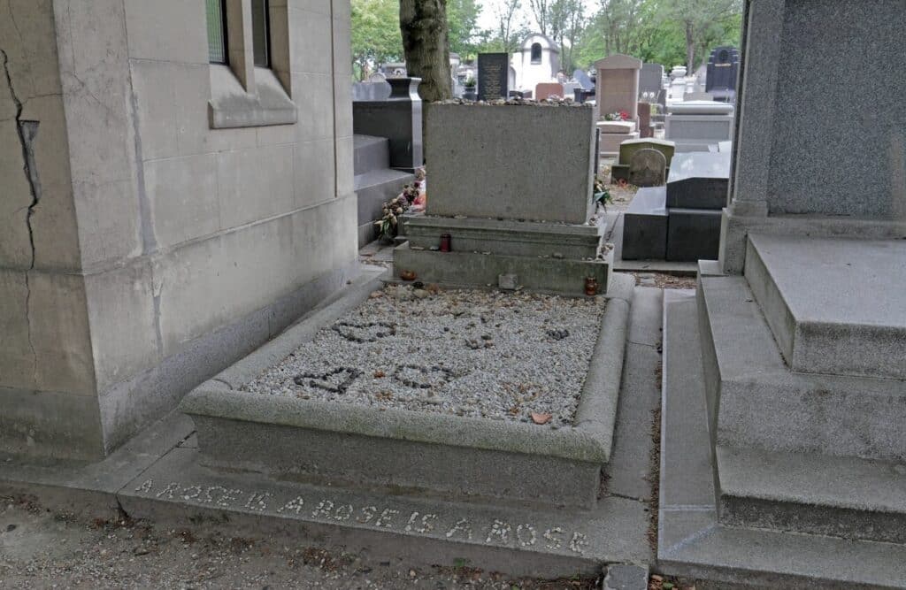 The minimalist grave of writer Gertrude Stein at Père Lachaise Cemetery is covered in small stones, with her famous phrase "A rose is a rose is a rose" engraved along the edge, honoring her literary legacy.