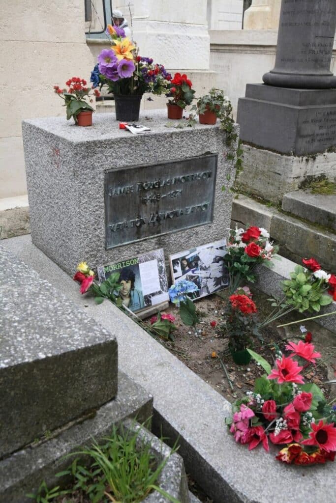 The grave of Jim Morrison at Père Lachaise Cemetery is adorned with colorful flowers, photographs, and fan tributes honoring the legendary singer of The Doors.