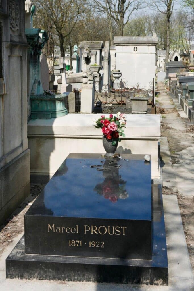 The sleek black tomb of Marcel Proust at Père Lachaise Cemetery bears his name in gold lettering and is adorned with a vase of red roses, reflecting the quiet reverence for the celebrated French writer.