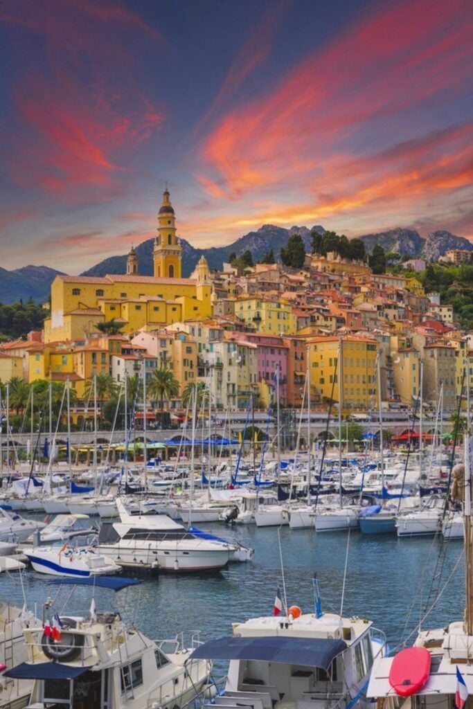 A stunning sunset casts vibrant hues over Menton’s Old Town and marina, where colorful buildings and docked sailboats create a postcard-perfect scene—one of the most breathtaking things to do in Menton France.