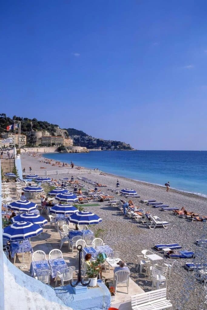The famous pebble beaches of Nice, lined with blue-and-white umbrellas and sun loungers, offer a perfect spot to relax by the Mediterranean—one of the most classic things to do in Nice for sunseekers and beach lovers.
