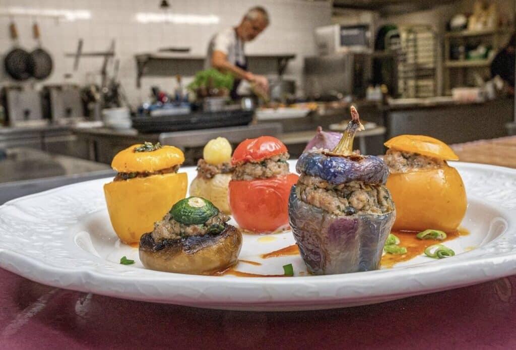 Colorful petits farcis, a signature dish of cuisine niçoise, featuring vegetables stuffed with seasoned meat, served on a white plate in a traditional French kitchen.