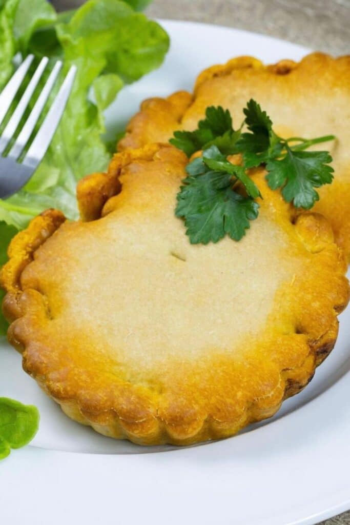 Tasting local cuisine is one of the best things to do in Montpellier, and the region’s signature *petit pâté de Pézenas* is a must-try. This image showcases two golden, flaky meat pies garnished with fresh parsley, served alongside crisp lettuce for a delicious and authentic culinary experience.
