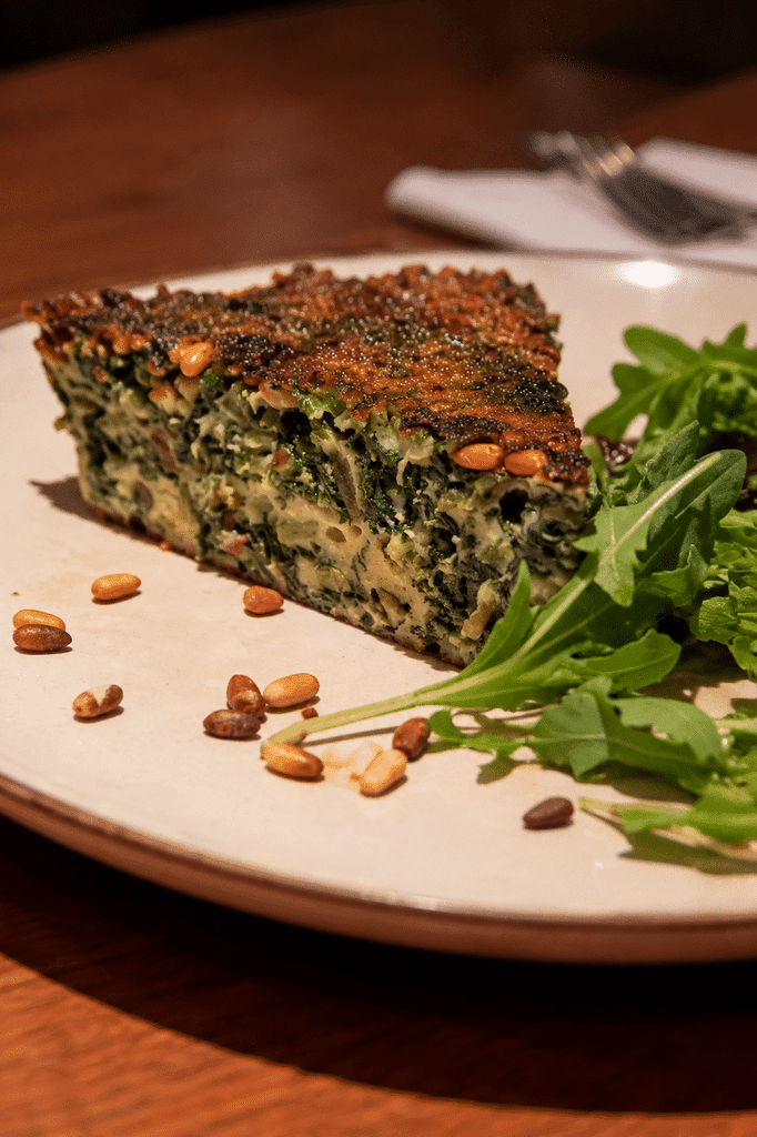 Traditional Trucha (Trouchia) Niçoise, a thick Swiss chard omelet with a golden-brown crust, served with fresh salad greens and toasted pine nuts in Nice, France.