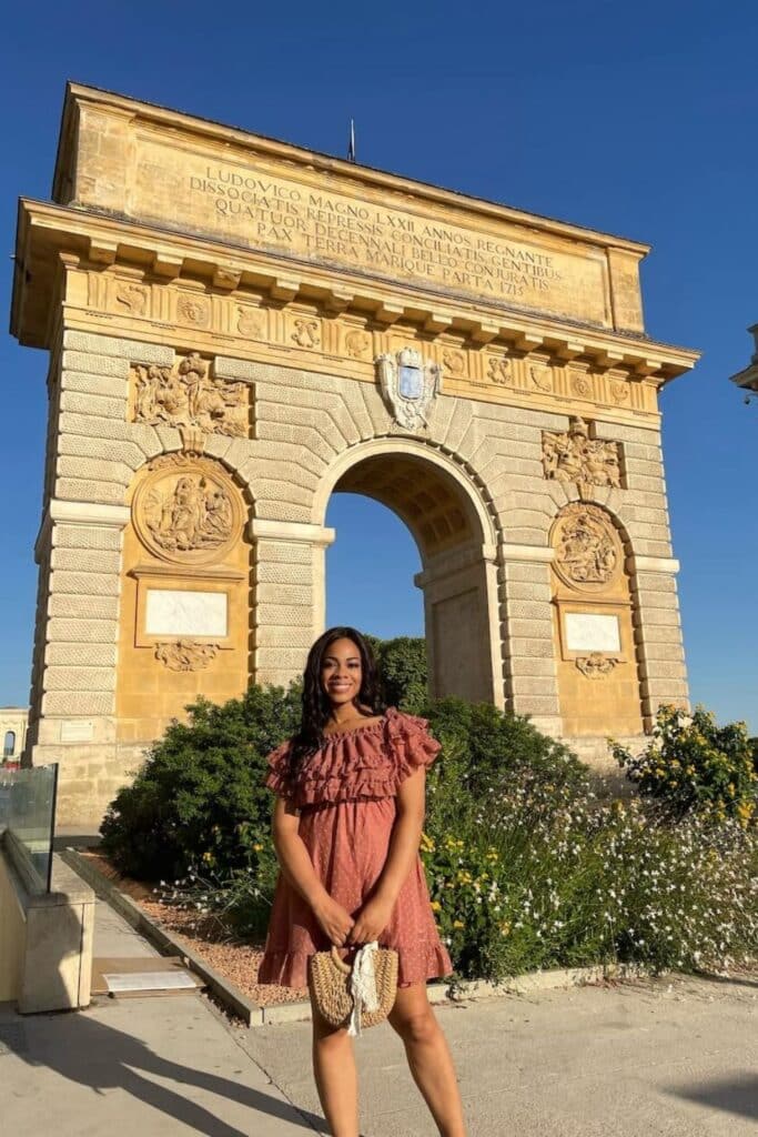 A visit to the Arc de Triomphe is one of the top things to do in Montpellier, offering a glimpse into the city's rich history and stunning architecture. In this image, a woman poses in front of the grand monument, bathed in warm sunlight, making for a perfect sightseeing moment.