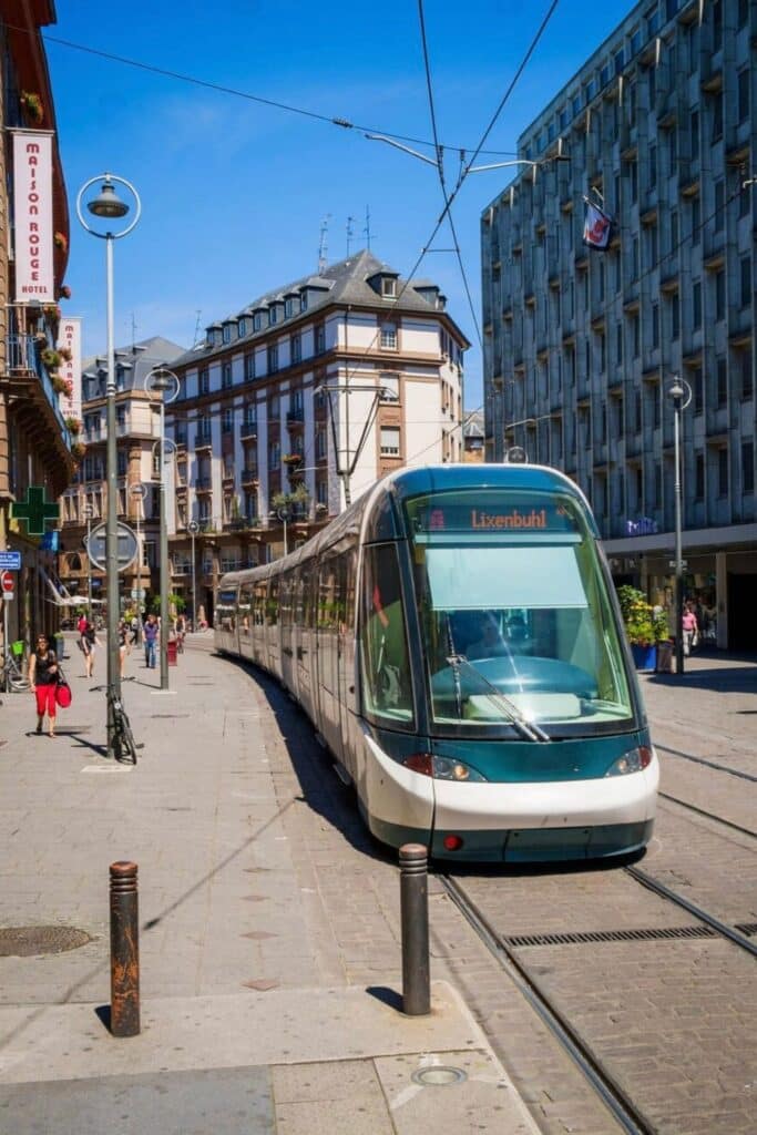 A modern tram in Strasbourg, France, passing through the historic city center near Maison Rouge Hotel on a sunny day. This efficient public transport is a great way to explore the city during a one-day in Strasbourg itinerary.