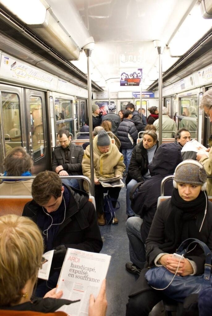 Passengers sitting and standing inside a crowded Paris metro car, showing what it’s like when learning how to use the metro in Paris.