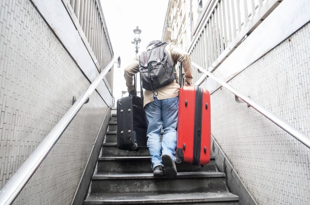 Traveler carrying two suitcases up the stairs while exiting a Paris metro station, showing the challenge of luggage when learning how to use the metro in Paris.