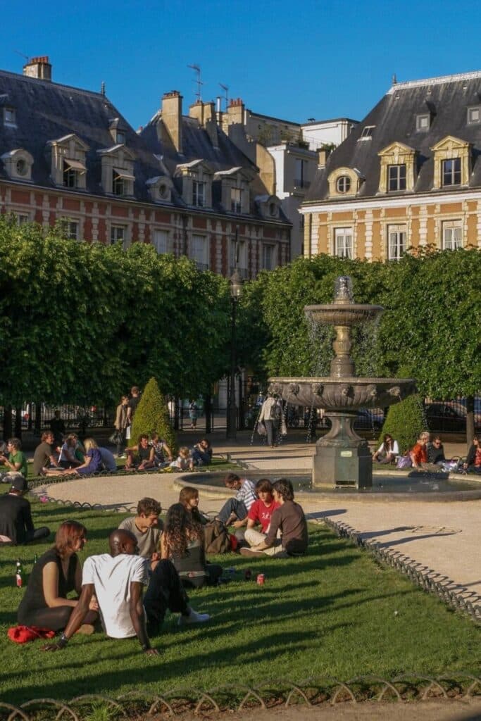 Groups of friends relaxing by the fountain at Place des Vosges in Le Marais—an ideal setting when deciding where to stay in Paris for historic charm, cozy gardens, and a lively yet elegant neighborhood atmosphere.