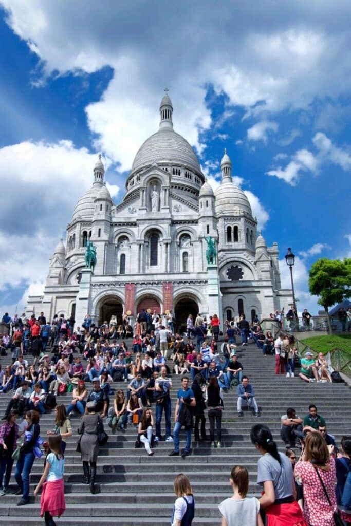 Crowds gathered on the steps of Sacré-Cœur Basilica in Montmartre, enjoying panoramic views of Paris—an unforgettable setting when choosing where to stay in Paris for artistic charm and iconic hilltop scenery.