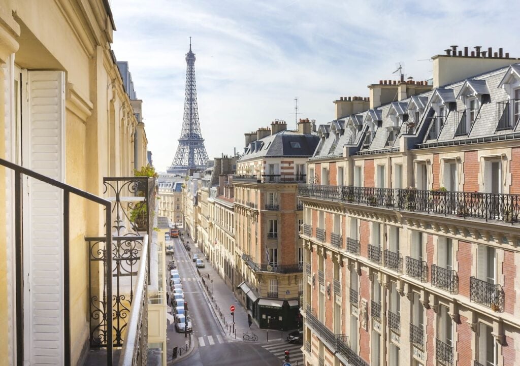 Balcony view from Hôtel Élysées Union overlooking a Paris street with classic buildings and the Eiffel Tower in the distance, ideal for cheap hotels with Eiffel Tower view.